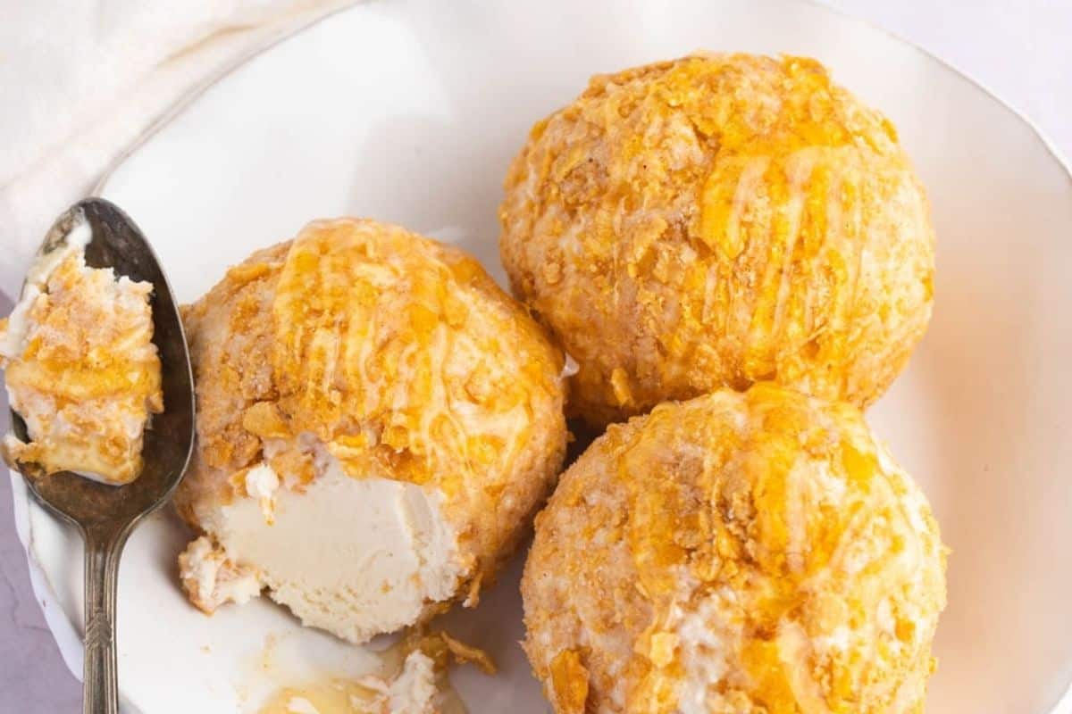 Three scoops of fried ice cream topped with a golden coating, served in a white bowl, evoke a fiesta of flavors. Perfect for Cinco de Mayo celebrations, this dessert brings joy to any occasion with its delightful contrast of textures.