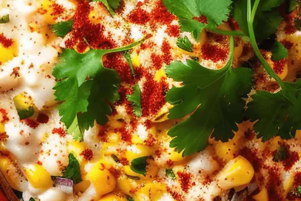 Close-up of a flavor-packed party dip featuring corn, red chili powder, and fresh cilantro leaves, with a creamy sauce visible underneath—a vibrant addition for Cinco de Mayo celebrations.