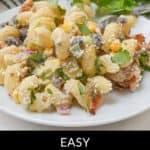 A plate of Mexican Street Corn Pasta Salad brimming with pasta, corn, black beans, and cilantro. A slice of lime and fresh herbs in the background enhances the vibrant dish. Text overlay: "Easy Mexican Street Corn Pasta Salad.