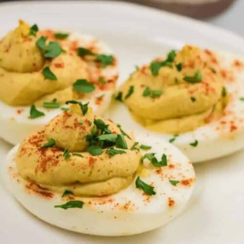 Three deviled eggs on a plate, topped with paprika and chopped parsley, make the perfect Easter side dish.