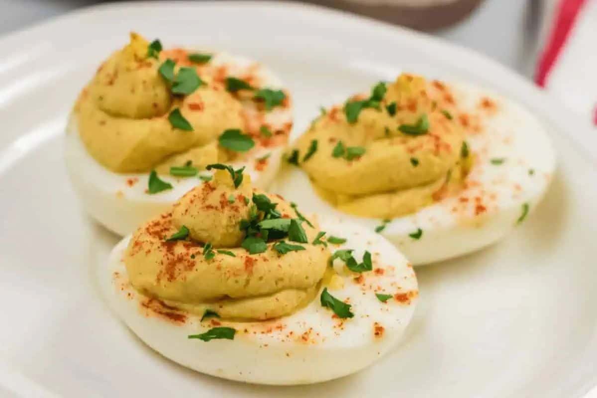 Three deviled eggs on a plate, topped with paprika and chopped parsley, make the perfect Easter side dish.