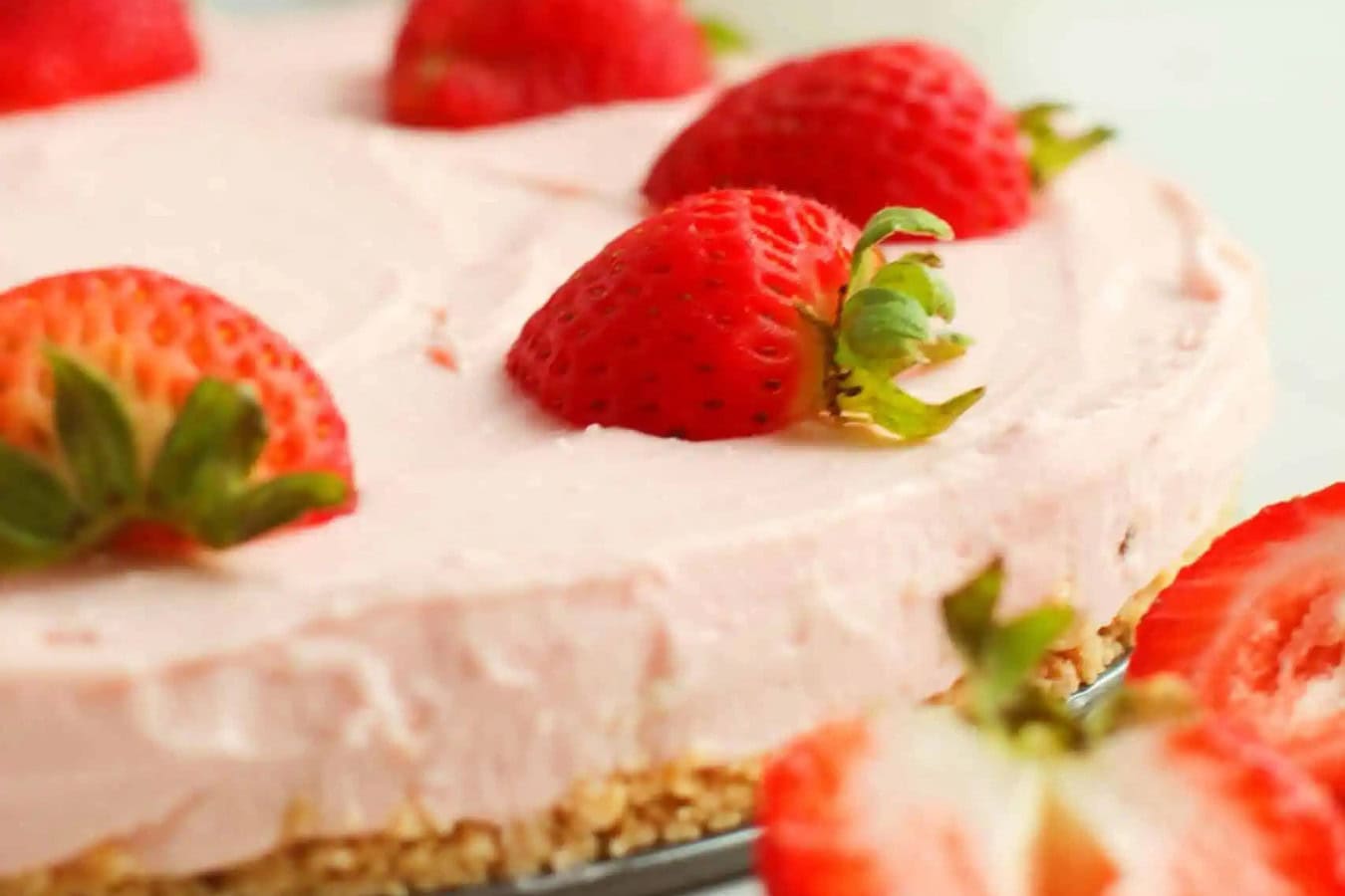 Strawberry cheesecake with a pink filling on a crumbly base, topped with halved strawberries. This spring dessert is not only beautiful but truly tastes as good as it looks.
