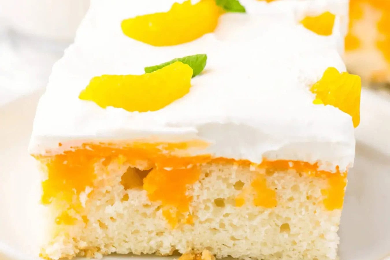 A slice of orange creamsicle cake with white frosting and orange slices on top showcases a moist interior with visible orange filling, making it one of the most beautiful spring desserts to taste.