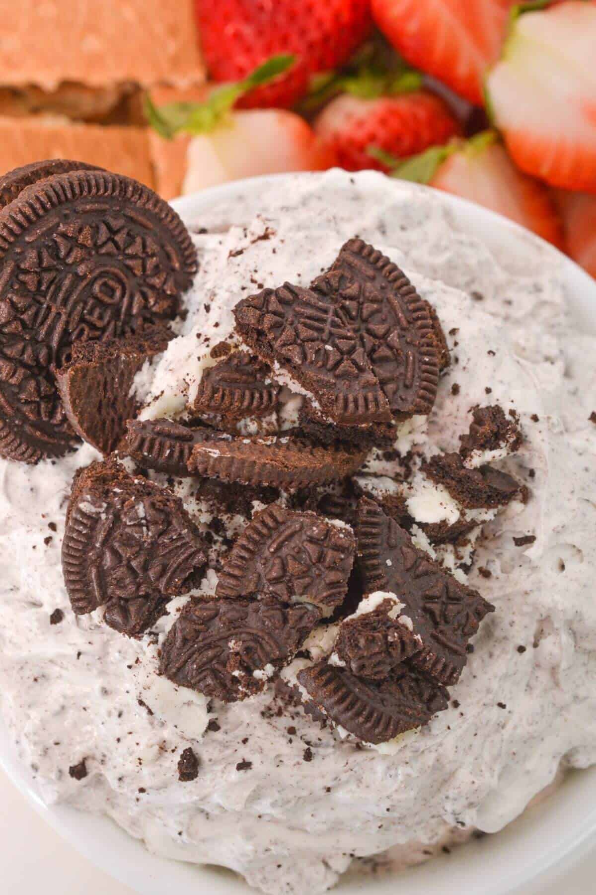 A close-up of a luscious Oreo Dip, adorned with crushed chocolate sandwich cookies. In the background, juicy strawberries and crispy graham crackers await their turn for a delightful dip.