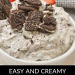Close-up of a bowl filled with creamy Oreo Dip topped with crushed Oreo cookies. Sliced strawberries and a gray cloth add a touch of elegance in the background. Text at the bottom reads "Easy and Creamy Oreo Dip.