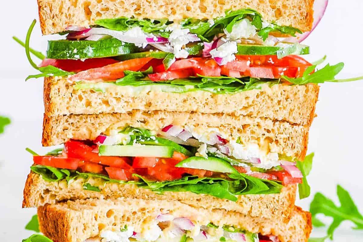 Panera Mediterranean Veggie sandwich with whole grain bread, tomatoes, cucumbers, red onion, lettuce, and feta cheese, stacked to show the layers.
