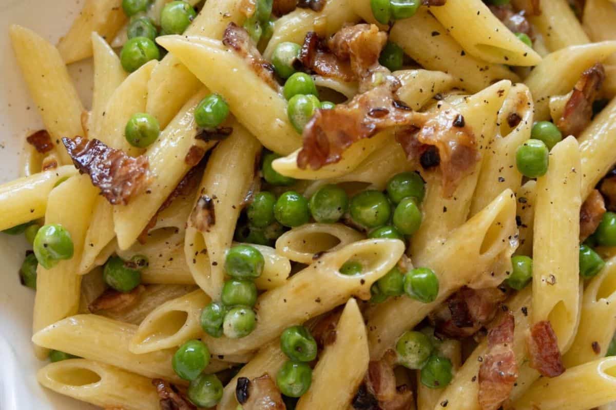 Spring into flavor with this delightful dish of penne pasta, featuring fresh green peas, crispy bacon, and a touch of black pepper.