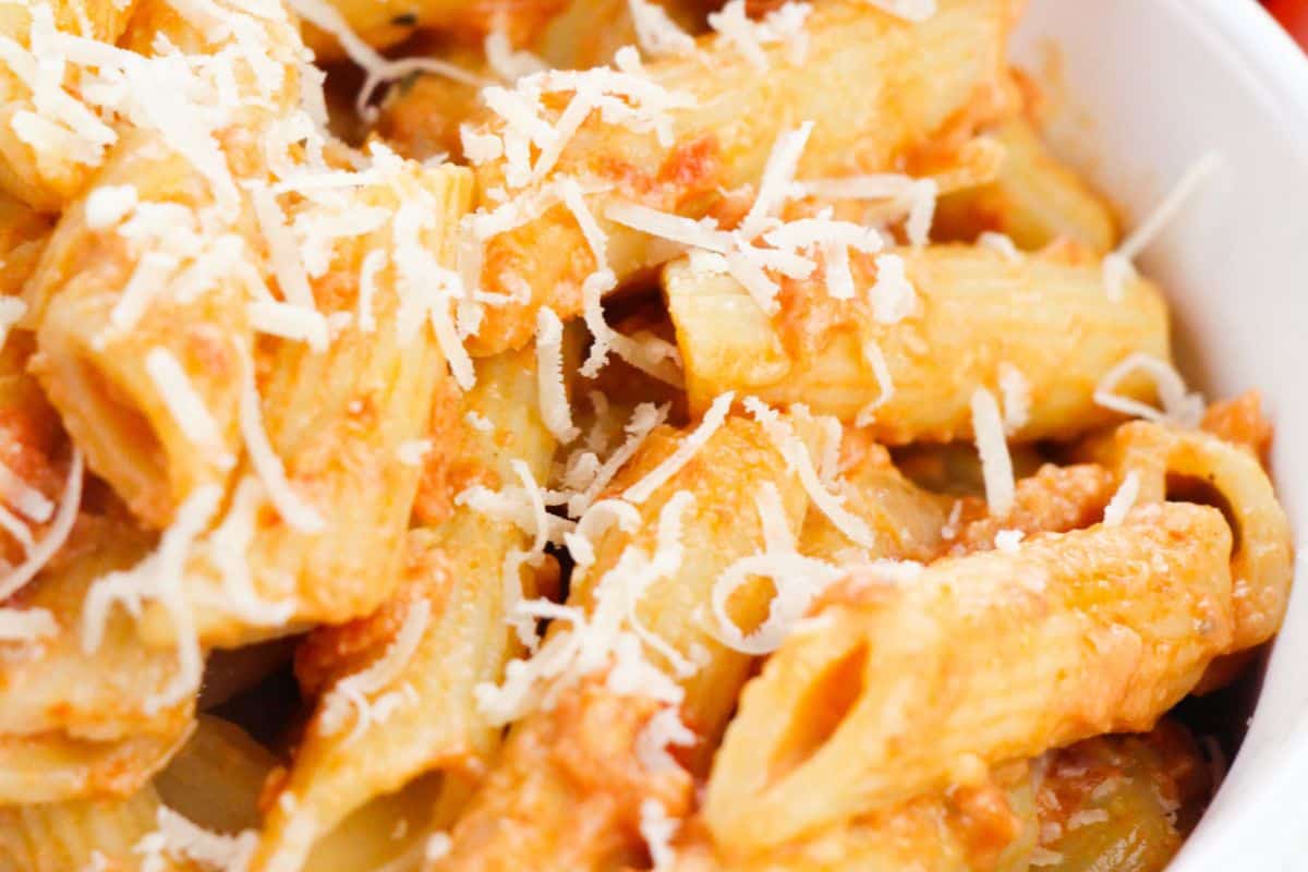 A must-try pasta dish: a close-up of rigatoni smothered in fresh vokda sauce and topped with grated cheese, perfect for any spring meal.