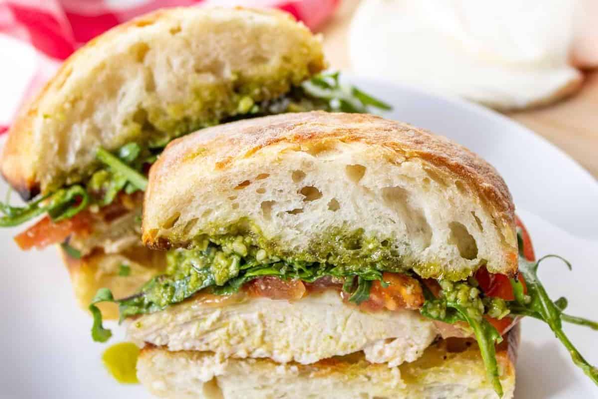 Pesto chicken sandwich with grilled chicken, pesto sauce, arugula, and tomato on a ciabatta roll.