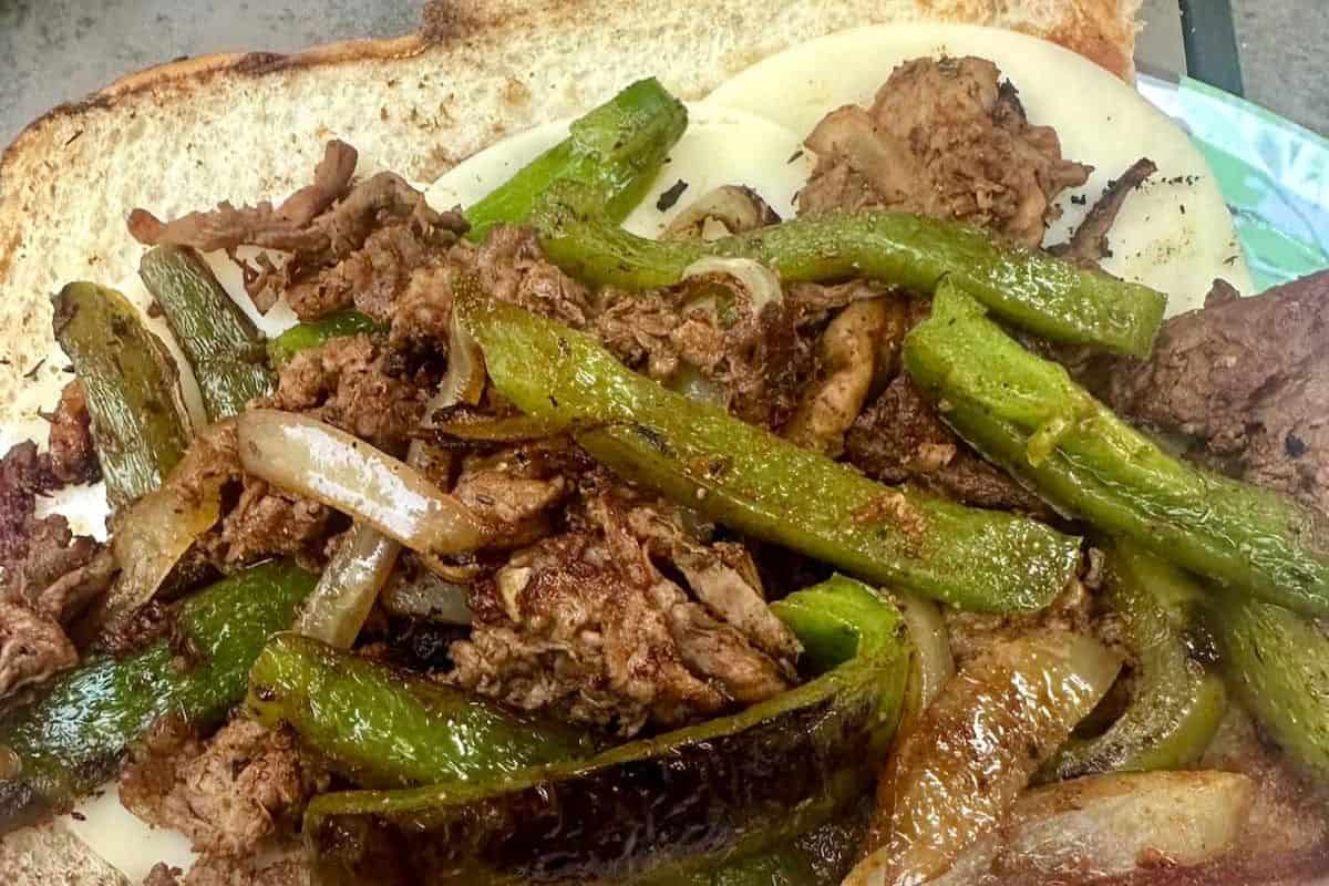 Philly cheesesteak sandwich with thinly sliced steak, sauteed onions, green bell peppers, and melted white cheese on toasted white bread.