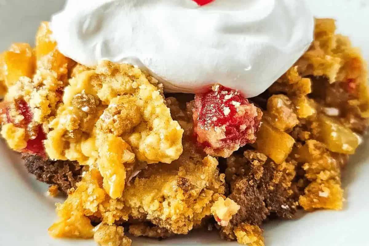A fiesta-worthy pineapple dump cake featuring a crumbly topping, vibrant red and yellow fruits, and a dollop of whipped cream on top. Perfect for celebrating Cinco de Mayo!.