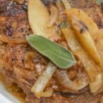 A white platter with pork chops and apples and onions.