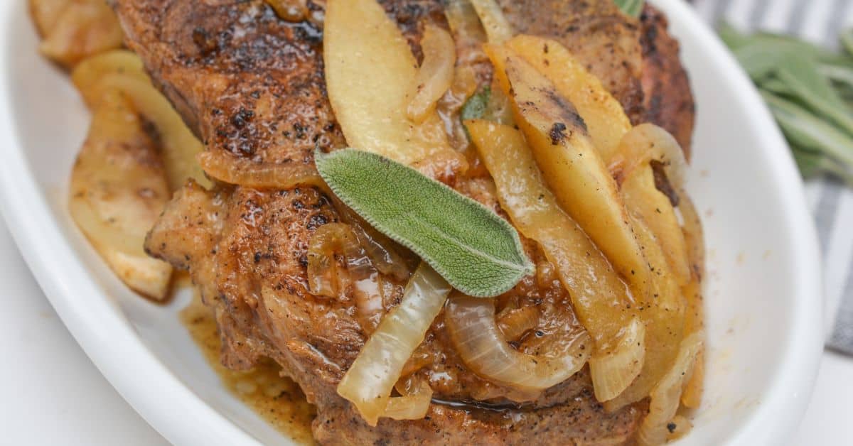 A white platter with pork chops and apples and onions.