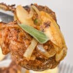 Tongs holding a piece of pork chops and apples and onions.