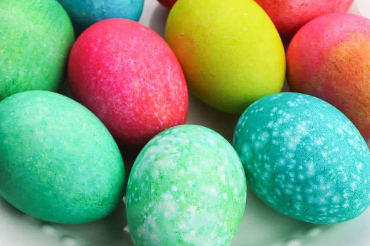 A close-up of brightly colored Easter eggs, showcasing creative ideas in shades of green, blue, pink, red, and yellow, arranged randomly on a white surface.