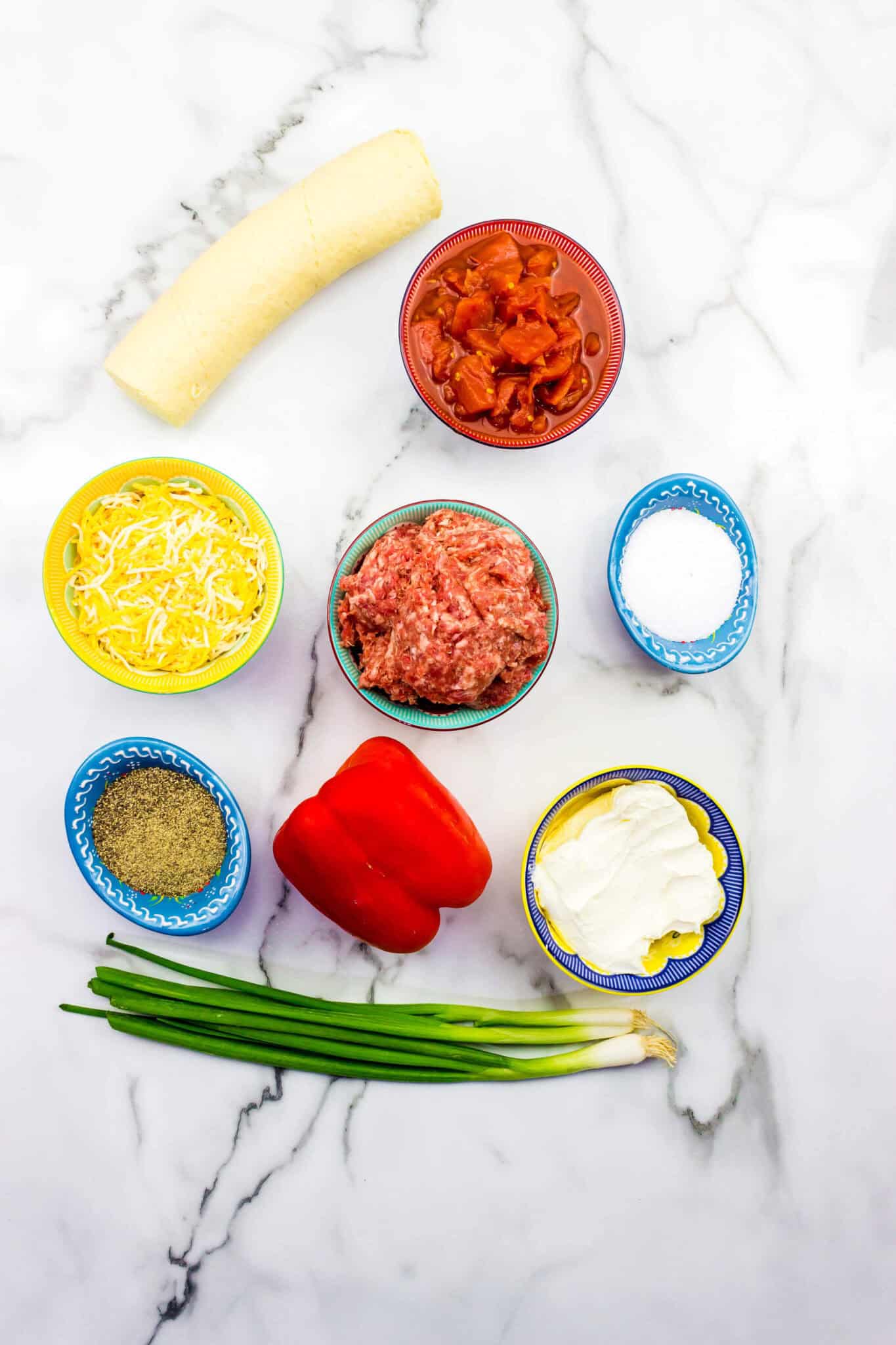 Ingredients arranged on a marble surface: crescent roll dough, diced tomatoes, shredded cheese, ground meat, salt, pepper, red bell pepper, cream cheese—and for a savory twist.