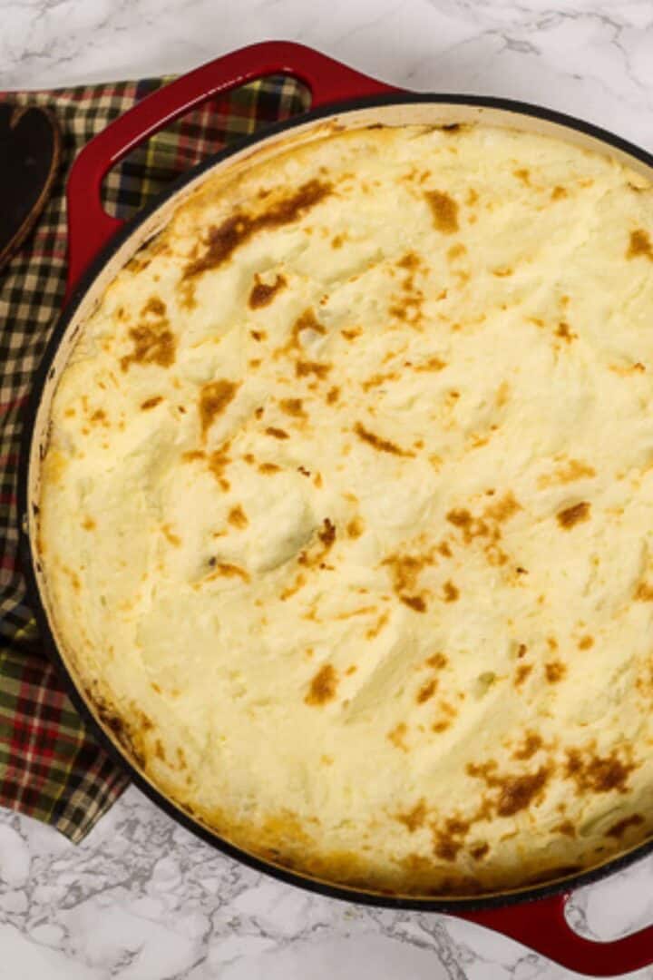 A shepherd’s pie with ground beef and a browned mashed potato topping in a red cast-iron skillet.