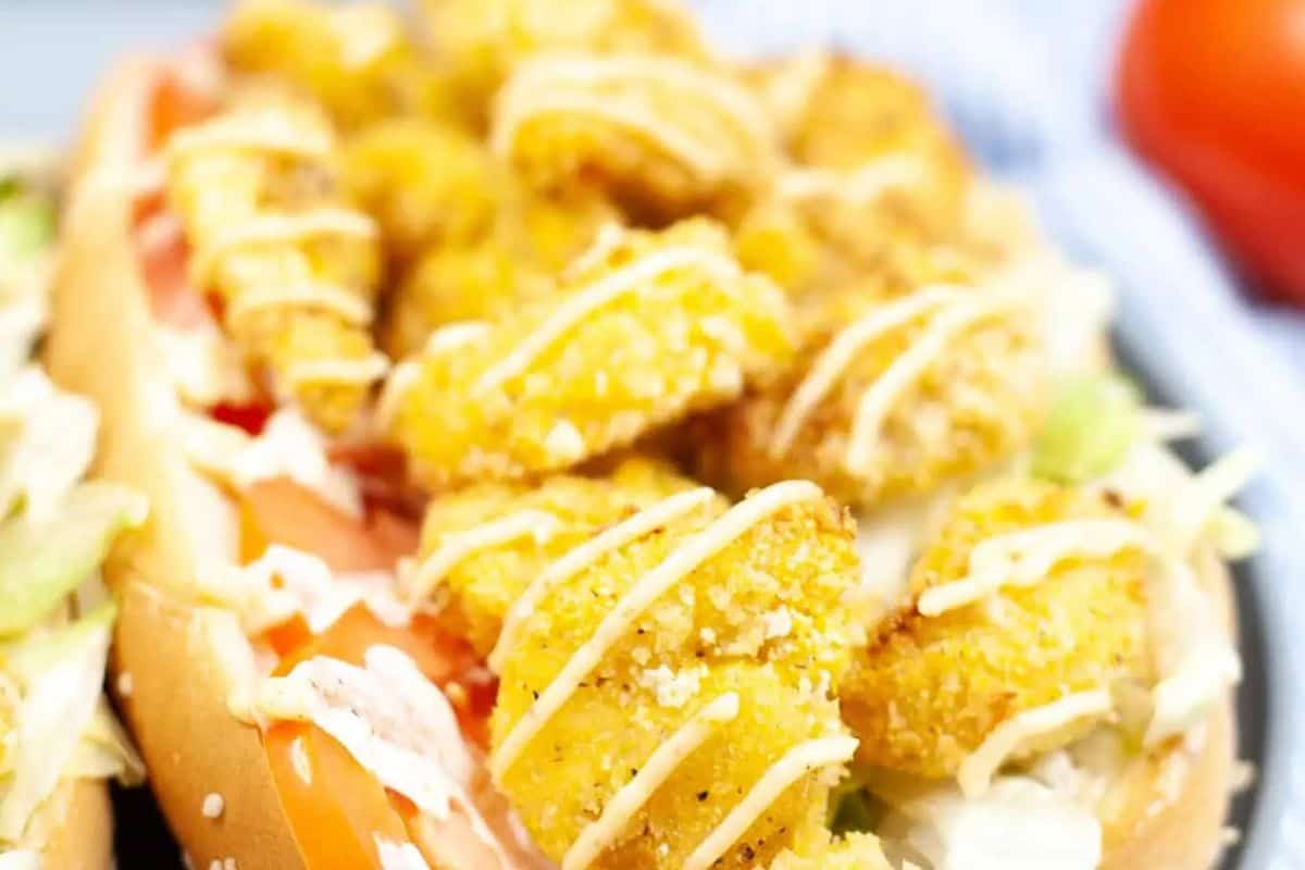 Shrimp po' boy sandwich with fried shrimp, tomato, lettuce, and a light drizzle of sauce in a long roll.
