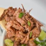 The dish garnished with chopped herbs on a wooden spoon, with lime wedges visible in the background.