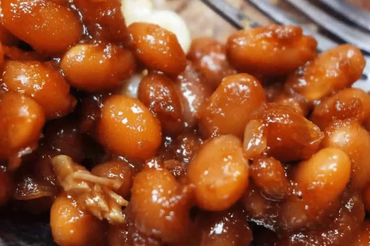 A close-up of baked beans in a rich, brown sauce showcases their glossy texture, with bits of meat nestled among them. This mouthwatering dish is perfect for delicious recipes that add comfort and warmth to any gathering.