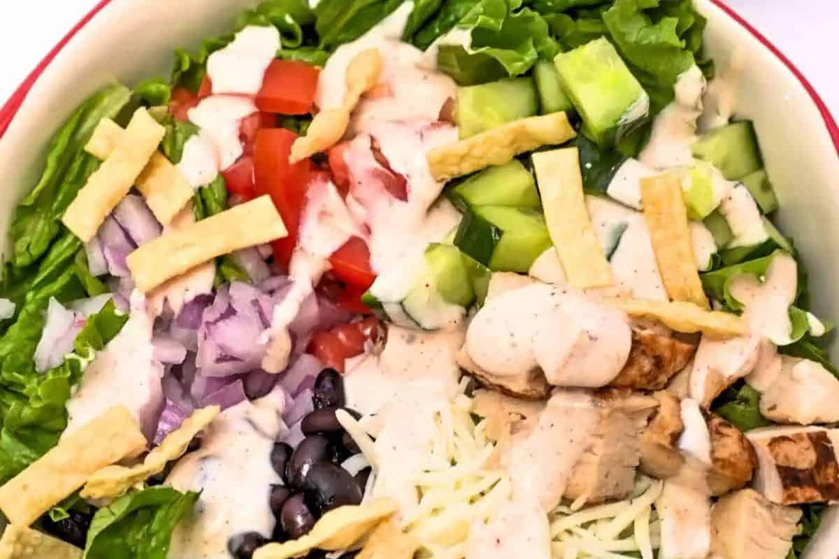 Introducing the best Spring Salad: A delightful mix of lettuce, diced tomatoes, cucumbers, red onion, black beans, and grilled chicken. Topped with shredded cheese and crunchy tortilla strips, all drizzled in a creamy dressing perfect for the season.
