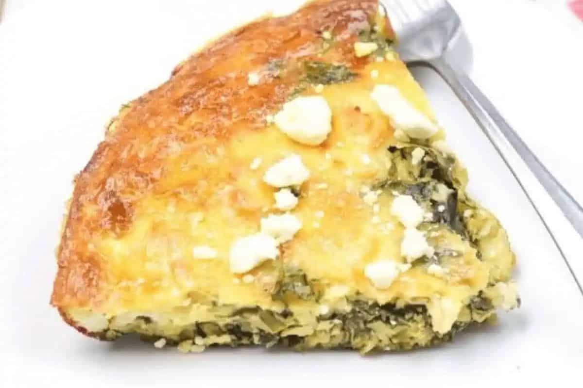 A perfect addition to your Easter brunch recipes, this slice of spinach and feta pie rests elegantly on a white plate, with a fork nearby.