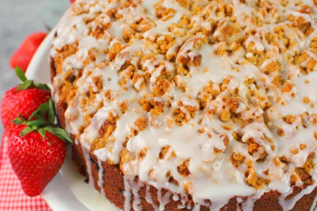 Savor this delightful coffee cake topped with streusel and icing, a perfect addition to your spring brunch recipes. Presented on a white plate alongside fresh strawberries, it promises to elevate your seasonal gatherings.