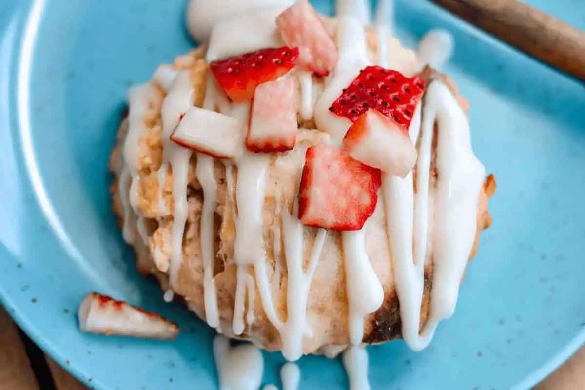 A delightful strawberry scone perfect for Easter Brunch Recipes, topped with white icing and vibrant strawberry slices on a charming blue plate.