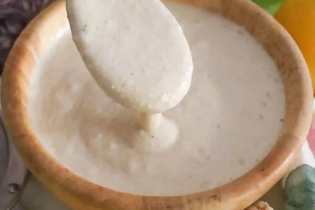 Creamy white Caesar salad dressing being scooped from a wooden bowl with a spoon, showing its thick texture.