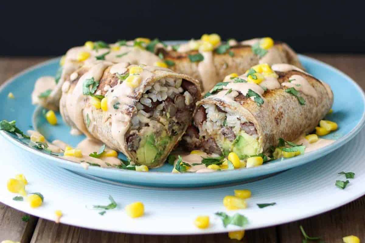 Homemade burritos topped with creamy sauce, garnished with cilantro and corn, are placed on a festive blue plate—perfect for your Cinco de Mayo celebration.