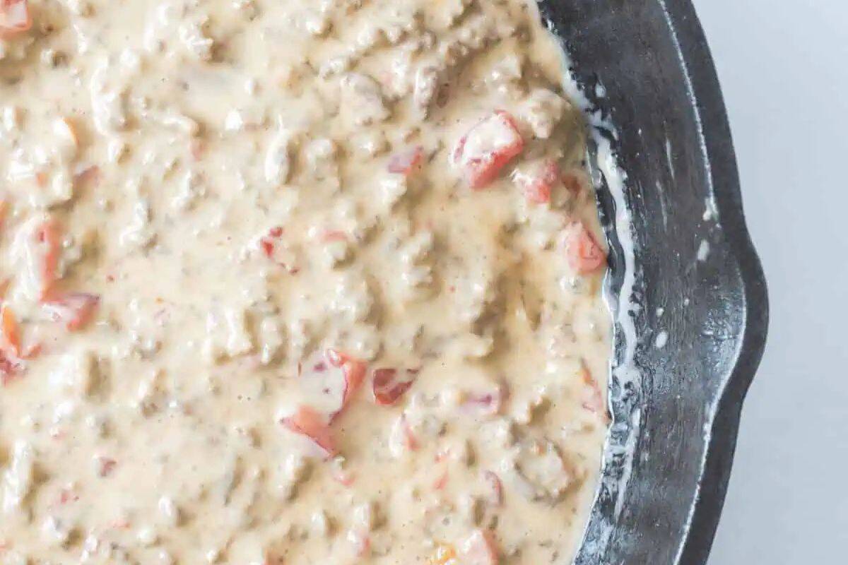 A close-up of a skillet holding a creamy velveeta rotel dip with ground meat and chopped red tomatoes, perfect for a Cinco de Mayo celebration.