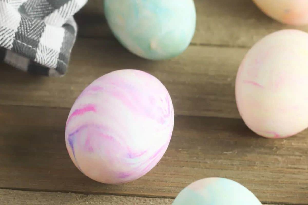Marble-patterned Easter eggs in pastel colors rest on a wooden surface beside a checkered cloth, showcasing creative ideas for Easter egg decorating.