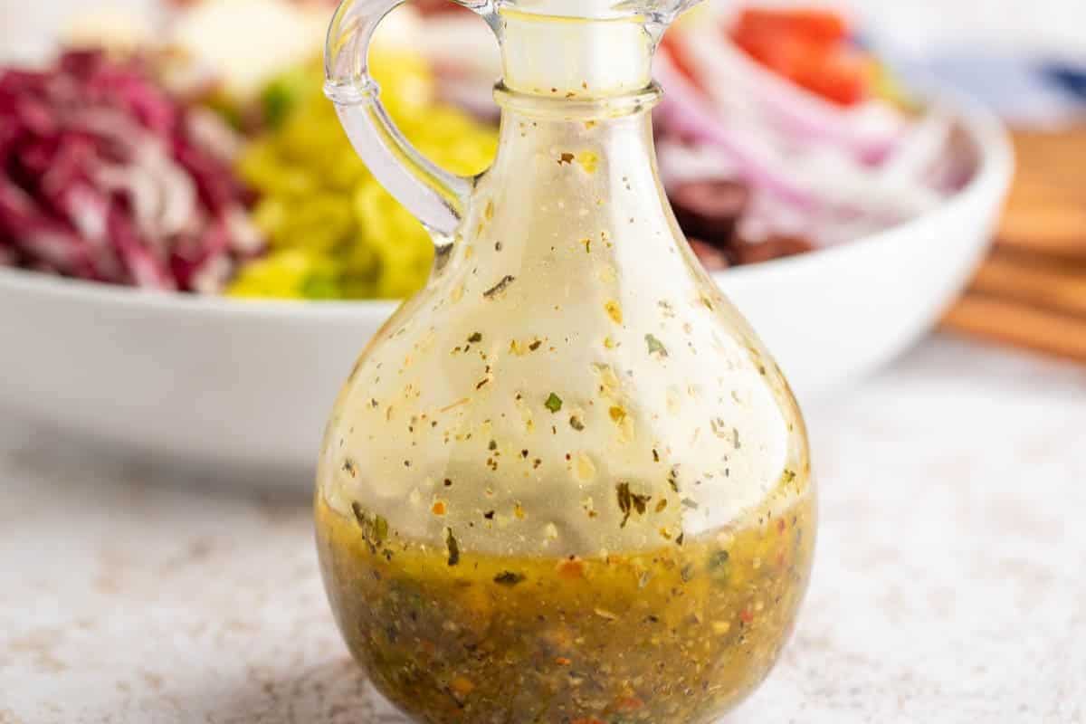 A glass jar filled with zesty Italian dressing, with visible herbs and spices.