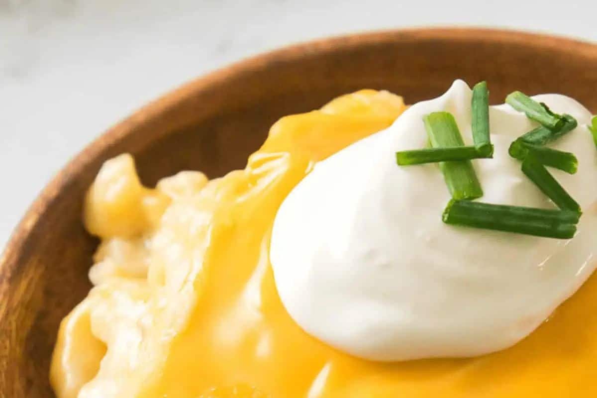 A bowl of macaroni and cheese topped with a dollop of sour cream and garnished with chopped chives—perfect for satisfying those comfort food cravings.