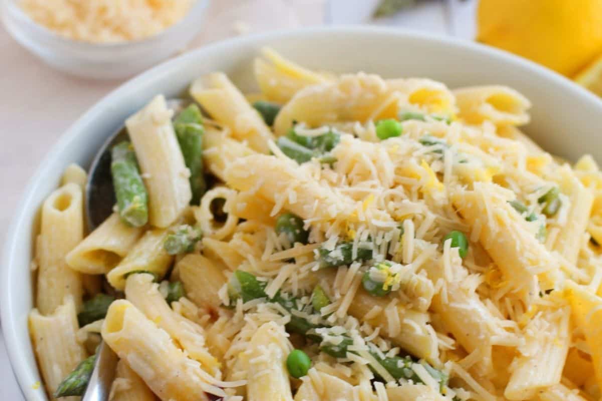 A Lent-friendly bowl of penne pasta mixed with asparagus and peas, topped with grated cheese, promises a delightful burst of flavor.