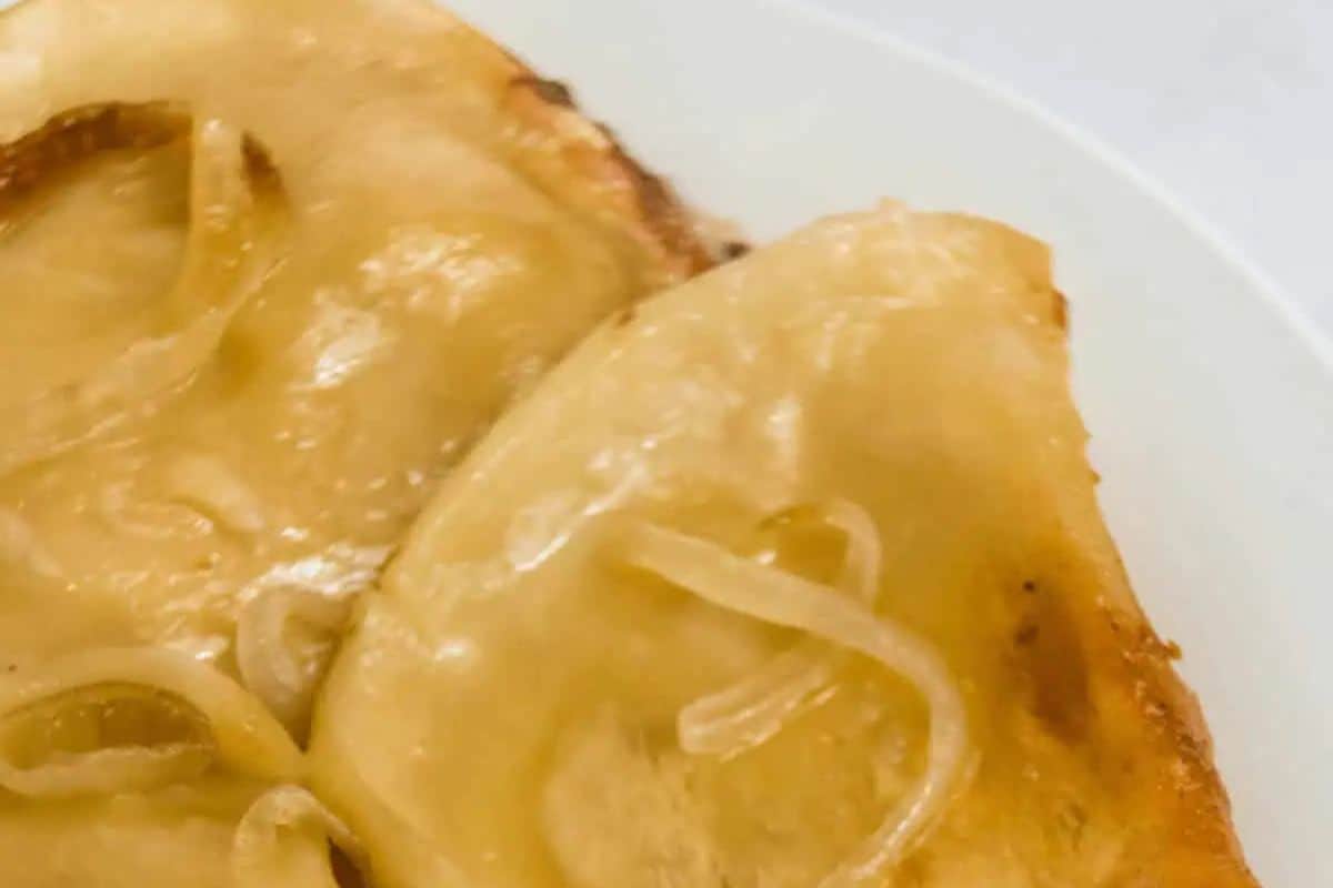 Two pieces of golden brown toast topped with melted cheese and thinly sliced onions on a white plate, perfect for satisfying your cravings.