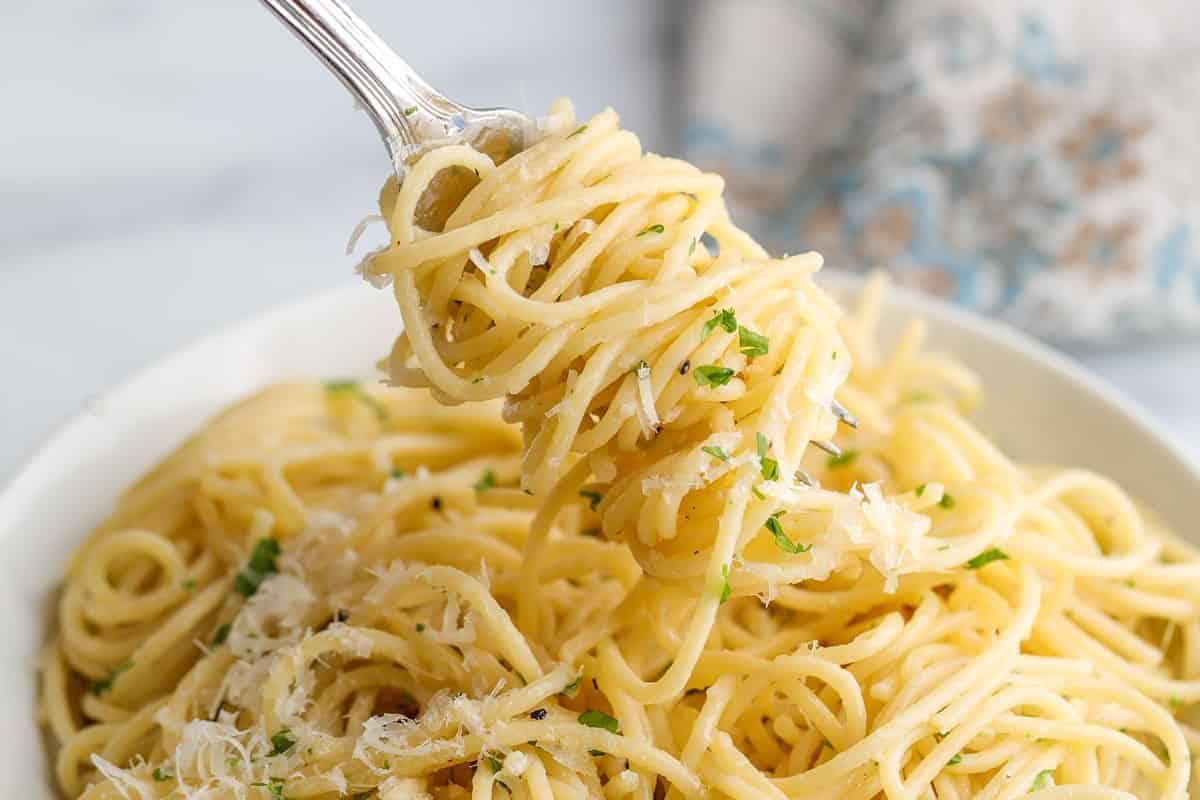 A fork twirls flavorful spaghetti topped with grated cheese and parsley, nestled in a white bowl. Perfect for those seeking Lent-friendly pasta recipes that are both delicious and satisfying.