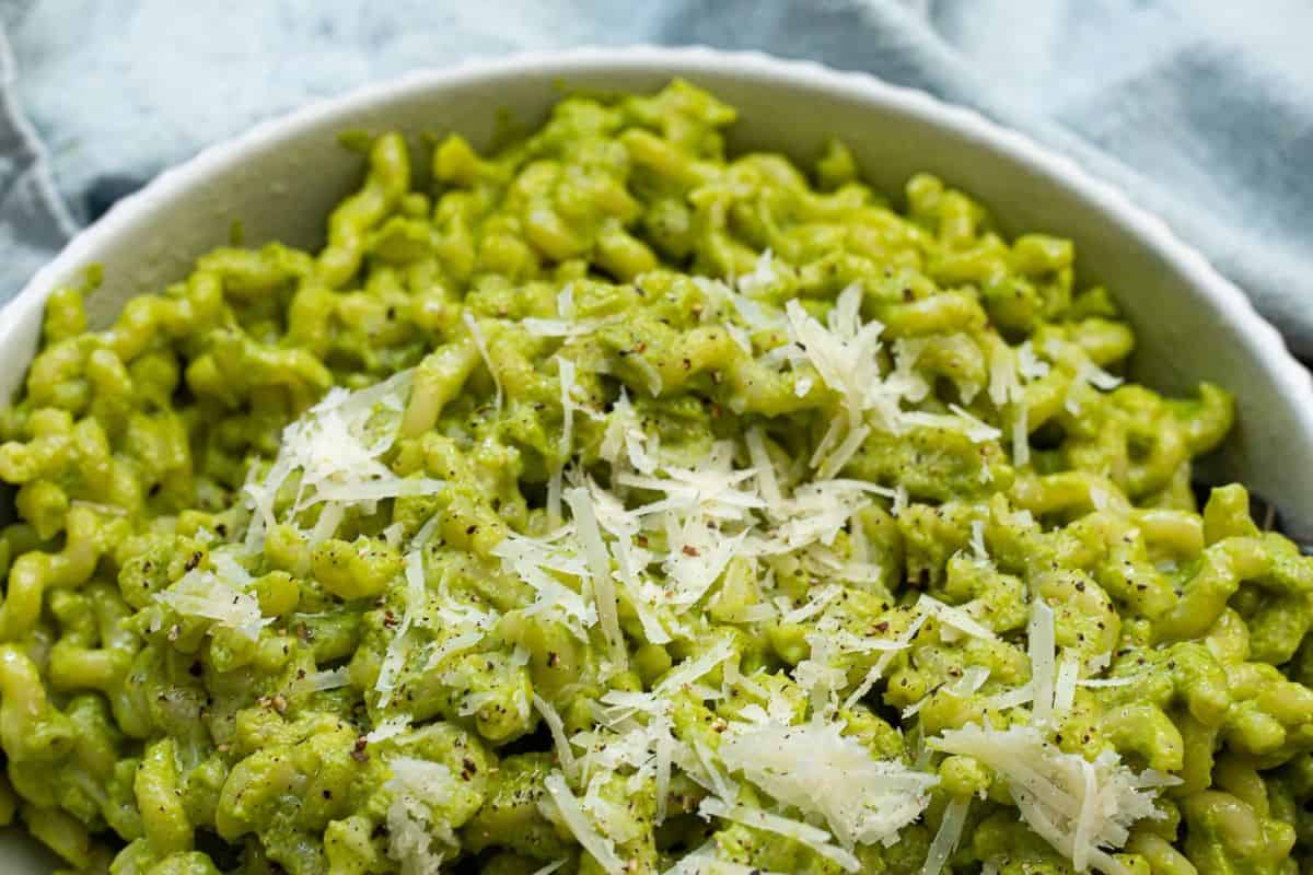 A twist on traditional mac and cheese, this dish features pasta coated in a vibrant green pesto-infused cheese sauce. Topped with grated Parmesan and black pepper, it has a rich, creamy texture with a fresh basil flavor.
