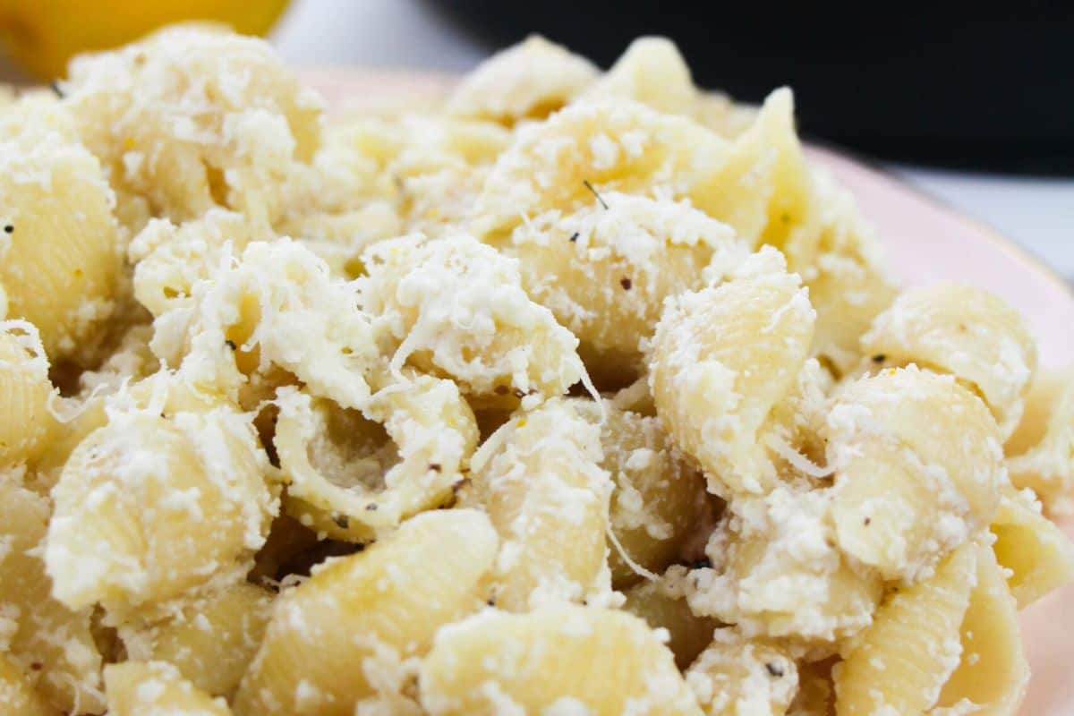 Close-up of cooked pasta shells coated in a flavorful, creamy white cheese sauce, lightly sprinkled with black pepper—a Lent-friendly delight.