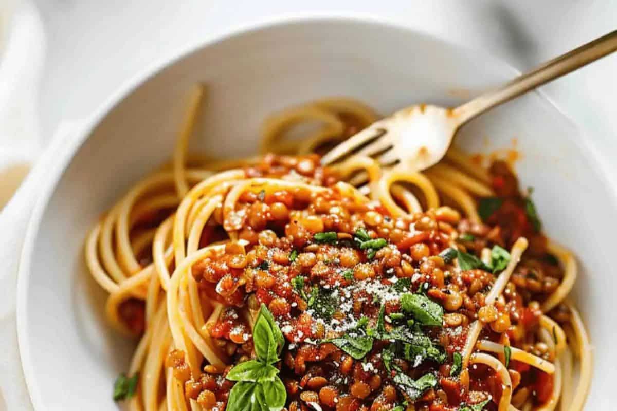A bowl of flavorful spaghetti topped with a rich tomato-based sauce, chopped herbs, and grated cheese, perfect for Lent-friendly pasta recipes. Accompanied by a fork.