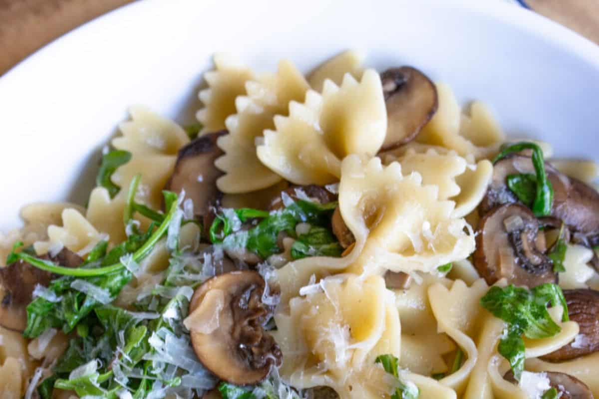 A flavorful, Lent-friendly pasta bowl featuring bowtie noodles topped with sliced mushrooms, grated cheese, and chopped greens.