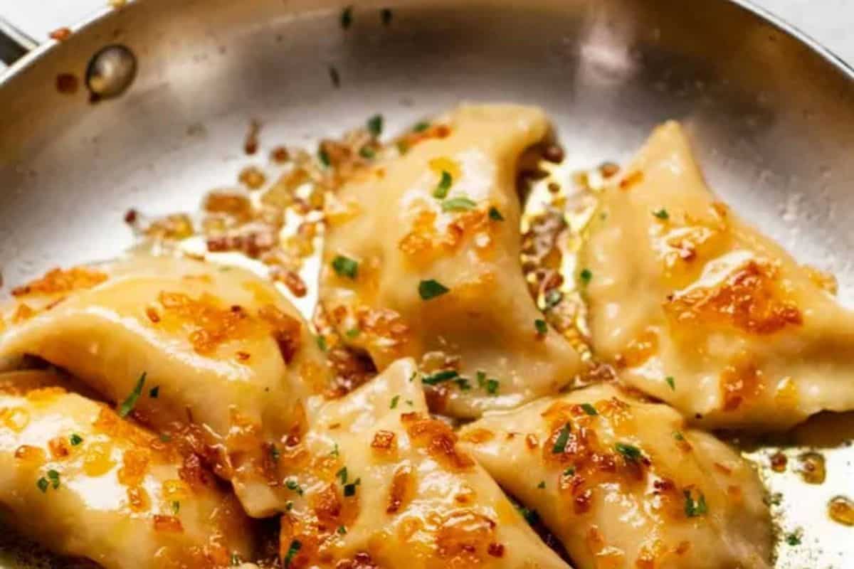 Several browned pierogi topped with sautéed onions and herbs in a metal skillet, satisfying even the most intense cravings.