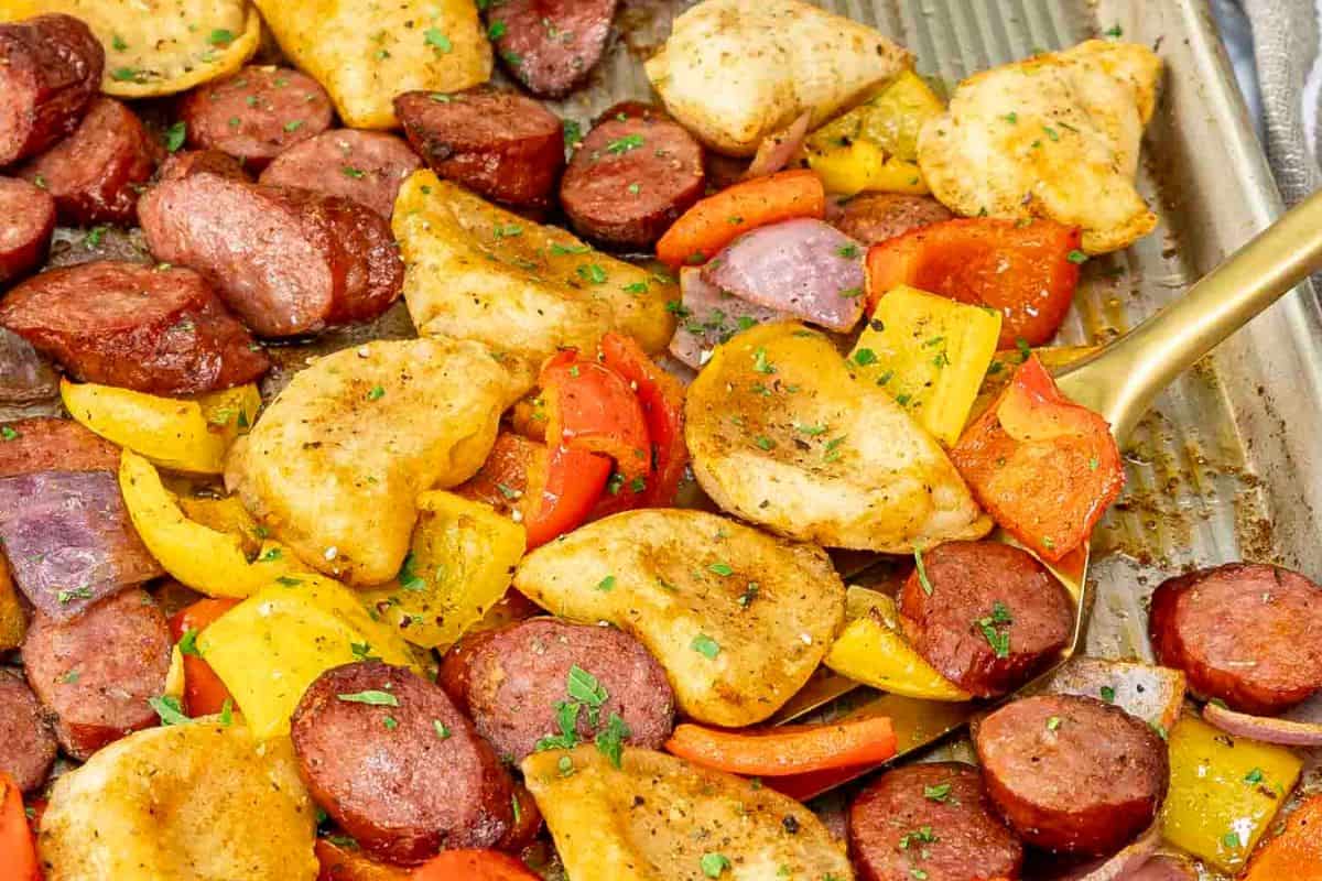 A sheet pan with sliced sausage, pierogi dumplings, and bell pepper pieces, seasoned and garnished with herbs offers a delightful dish that satisfies your cravings.