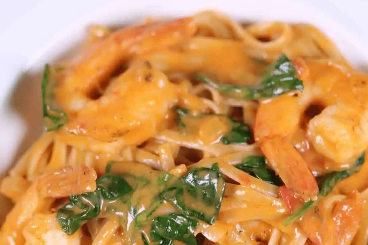A bold and creamy pasta dish featuring shrimp, fresh spinach, and a spicy, flavorful sauce coating fettuccine or linguine noodles. The rich, orange-hued sauce adds a delicious kick to this seafood favorite.