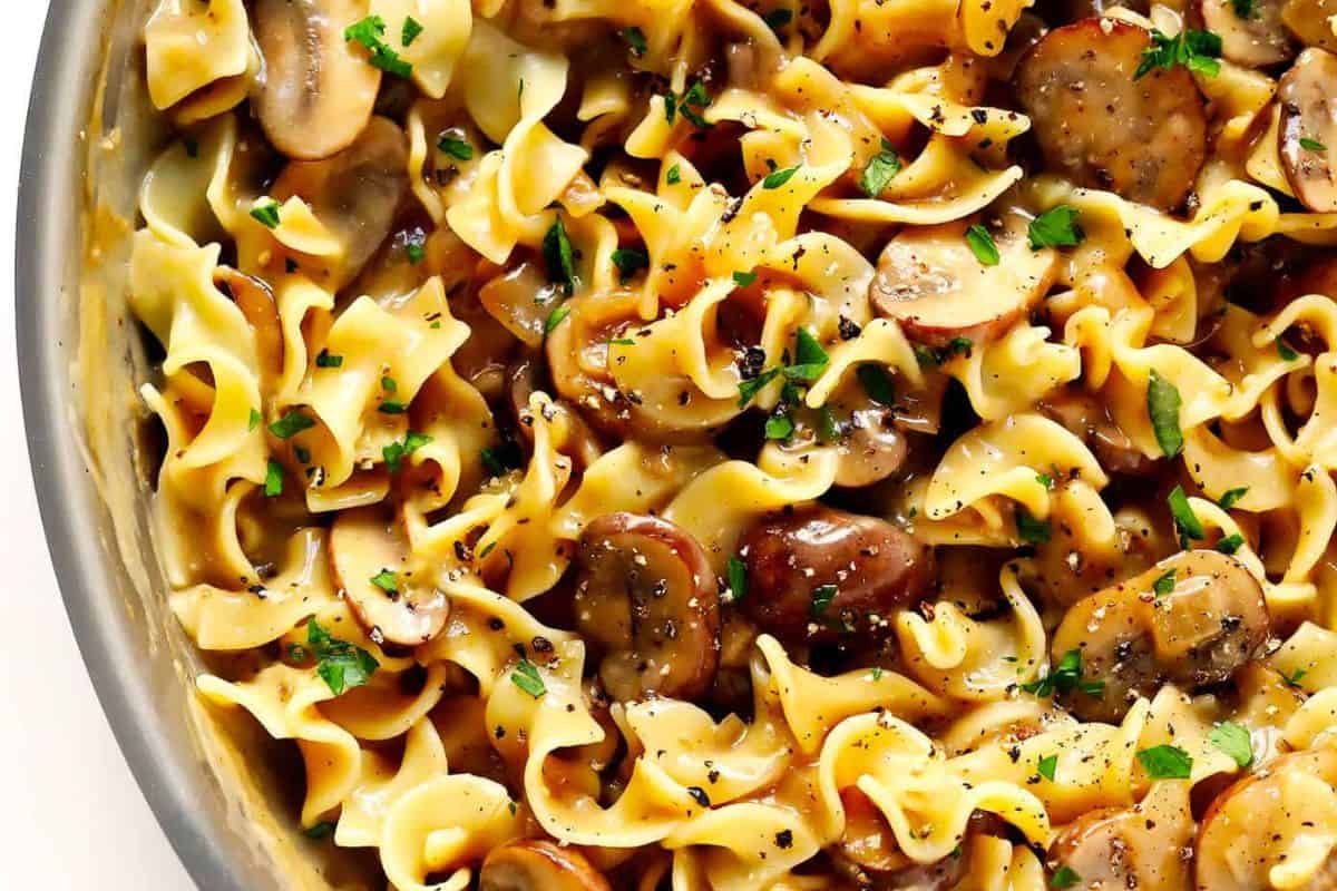 Close-up of cooked egg noodles mixed with sliced mushrooms, perfect for Lent or those seeking meatless recipes, garnished with chopped parsley and ground black pepper.