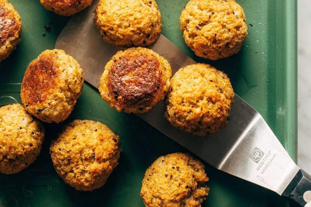 Several round, golden-brown baked falafel balls rest on a green surface, with a metal spatula lifting one piece—an ideal pick for those seeking delicious meatless recipes during Lent.