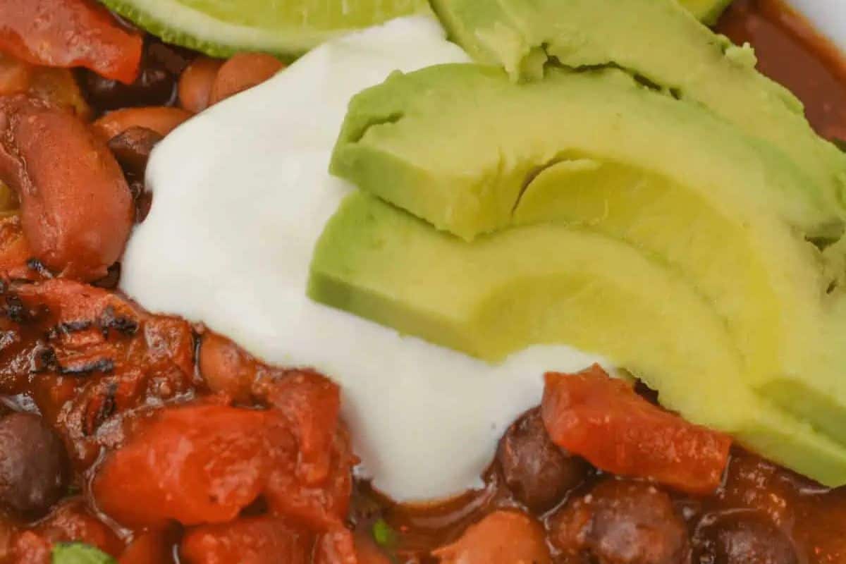 A close-up of chili beans and tomatoes, perfect for vegetarian meals, topped with a dollop of sour cream and sliced avocado.