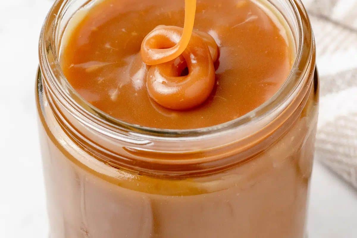 A close-up of a glass jar filled with creamy caramel sauce, with a swirl of caramel drizzled on top—perfect for easy caramel recipes and indulgent desserts.