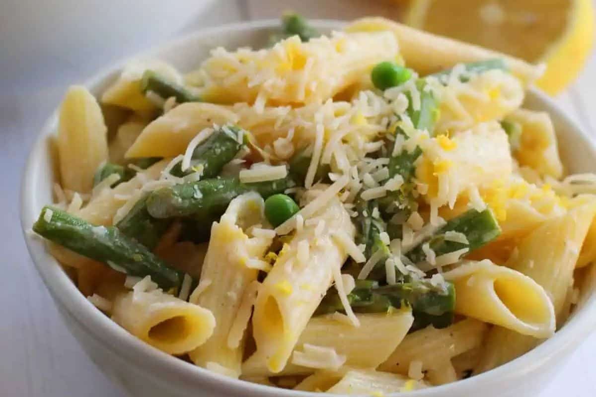 A bowl of penne pasta mixed with green beans, peas, and grated cheese, with a lemon wedge in the background—perfect for those seeking delicious Lent recipes.