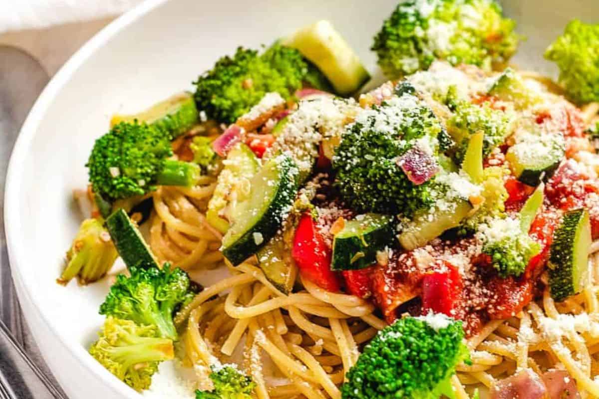 A plate of spaghetti topped with broccoli, zucchini, red onions, tomatoes, and grated Parmesan cheese—perfect for those seeking delicious Lent recipes or satisfying meatless meals.